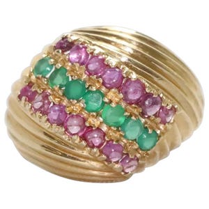 May include: A gold ring featuring a wide, ribbed band with a central row of round green gemstones flanked by two rows of round pink gemstones. The stones are set in a vertical pattern across the top of the band, creating a textured, multi-colored appearance.