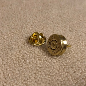 May include: A pair of gold-colored bullet casing earrings. The casings are marked "FEDERAL" and "7.62 AUTO 57".