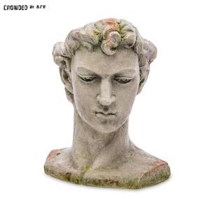 Puede incluir: Un busto de piedra gris desgastado de una persona con un peinado corto y rizado. El busto carece de la parte inferior del cuerpo y tiene una superficie rugosa y texturizada.