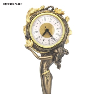 May include: A gold and bronze clock with a Roman numeral face and a decorative figure of a woman holding the clock. The clock is surrounded by gold leaves and flowers.