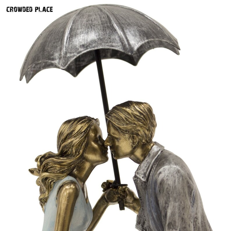 May include: A silver and gold-toned sculpture of a couple kissing under an umbrella. The sculpture is made of metal and has a realistic finish.