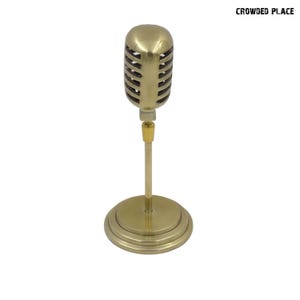 Może przedstawiać: Złoty metalowy mikrofon na stojaku. Mikrofon ma okrągłą głowicę z siatką z drutu. Stojak ma okrągłą podstawę.