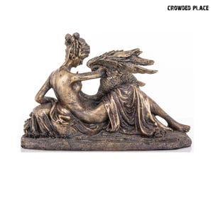 May include: A bronze sculpture of a woman reclining with a swan. The woman is nude and has her arm around the swan's neck. The swan has its wings spread out. The sculpture is on a brown base.