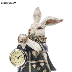 May include: White rabbit figurine with red eyes holding a gold pocket watch with roman numerals. The rabbit is wearing a green and gold vest with a heart pattern.