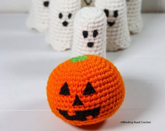 Puede incluir: Una calabaza naranja de ganchillo con una cara de calabaza negra se encuentra frente a una fila de cinco fantasmas blancos de ganchillo.