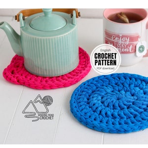 May include: Two crocheted coasters, one pink and one blue, with a teal teapot and a mug with the text "Enjoy Every Moment" on a white surface. The text "English Crochet Pattern PDF download" is also visible.