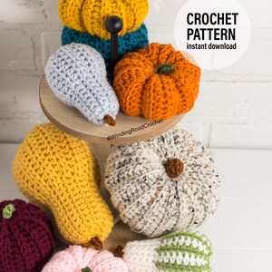 Puede incluir: Una colecci&oacute;n de calabazas y peras de ganchillo en varios colores, incluyendo amarillo, naranja, gris, blanco, verde y rosa. Las calabazas y las peras est&aacute;n dispuestas en un soporte de madera de dos niveles. La imagen incluye el texto "CROCHET PATTERN instant download".
