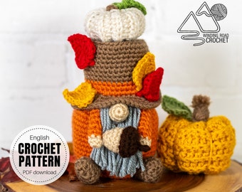 May include: Crocheted fall gnome with a pumpkin hat, holding a small acorn. The gnome is wearing a brown and orange sweater and a gray scarf. The gnome is sitting on a wooden surface next to a crocheted orange pumpkin. The text "English Crochet Pattern PDF download" is on a white circle.