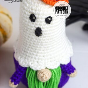K&ouml;nnte beinhalten: Geh&auml;kelter Geist-Zwerg mit einem orangefarbenen Hut mit violettem Rand. Der Zwerg hat einen violetten K&ouml;rper, einen gr&uuml;nen Bart und eine braune Nase. Der Text "English Crochet Pattern PDF download" befindet sich auf einem wei&szlig;en Kreis.