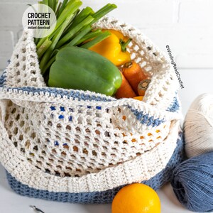 May include: A white crochet mesh bag with blue trim filled with spring onions, yellow and green peppers, carrots, and an orange. The bag is sitting on a white surface with two balls of yarn, one white and one blue.