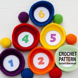 Peut inclure: Un ensemble de six paniers en crochet colorés avec les chiffres de 1 à 6. Les paniers sont disposés en forme de triangle. Il y a aussi six balles en crochet colorées assorties aux paniers.