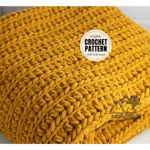 May include: A close-up of a mustard yellow crocheted blanket. The blanket is folded in half and the texture of the crochet stitches is visible. The text "English Crochet Pattern PDF download" is visible in a circle on the blanket.