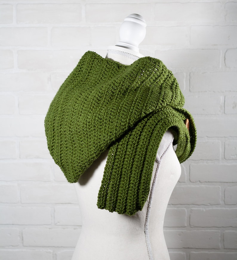 May include: A green crocheted cowl with a long, flowing end. The cowl is draped over a white mannequin.