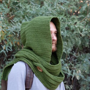 May include: A green crocheted hooded scarf with a wooden button. The scarf is worn by a person with a beard.