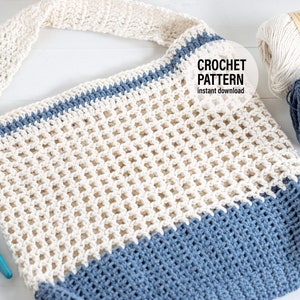 May include: A crocheted tote bag in a white and blue colour scheme. The bag has a wide, open top and a single strap. The bag is made with a mesh stitch and has a solid blue bottom. The bag is lying on a white surface with two balls of yarn in the background.