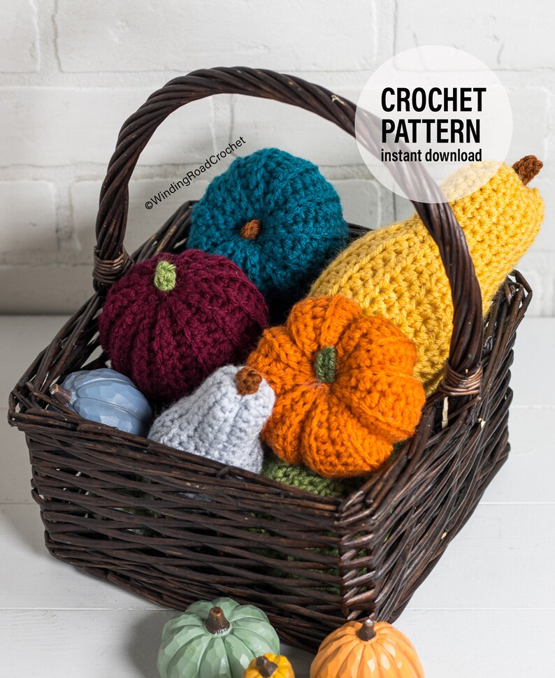 Puede incluir: Una cesta de mimbre llena de calabazas y calabacines tejidos a crochet en varios colores, incluyendo naranja, amarillo, turquesa, burdeos y gris. La cesta est&aacute; sobre una superficie blanca. El texto "CROCHET PATTERN instant download" es visible en la esquina superior derecha de la imagen.