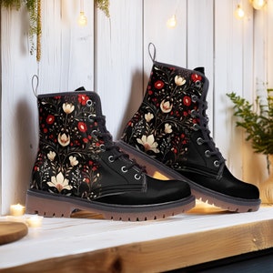 Puede incluir: Botas de cuero negro con estampado floral con flores rojas, blancas y doradas sobre fondo negro. Las botas tienen cierre de cordones y suela gruesa.