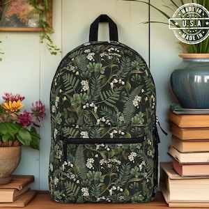 May include: A black backpack with a green and white floral pattern. The backpack has a zippered pocket on the front and two adjustable straps. The backpack is made in the USA.