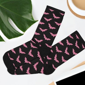 May include: A pair of black socks with a pink bat pattern. The socks are folded and displayed on a white surface.