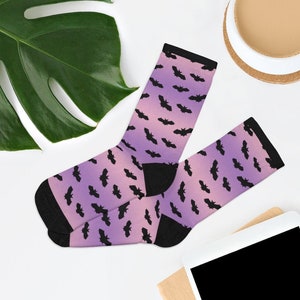 May include: A pair of socks with a pink and purple ombre gradient background and a black bat pattern.