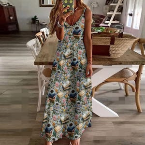 Puede incluir: Un vestido maxi azul claro con estampado floral y de libros. El vestido tiene un escote en V y tirantes finos.