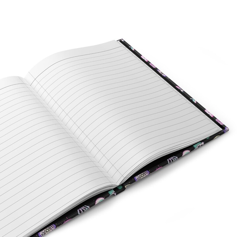 K&ouml;nnte beinhalten: Ein schwarzes Notizbuch mit einem bunten Muster aus Einh&ouml;rnern, Sternen und Regenb&ouml;gen auf dem Einband. Das Notizbuch ist ge&ouml;ffnet und zeigt linierte Seiten.