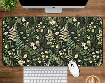 May include: A black and green mouse mat with a floral pattern featuring white flowers and green leaves. The mouse mat is on a wooden desk with a white keyboard, a white mouse, and a cup of coffee.