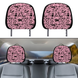 May include: Two pink car headrest covers with a black and white spooky Halloween pattern featuring ghosts, cats, bats, and witch hats.