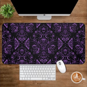 Könnte beinhalten: Eine schwarze und violette Schreibtischmatte mit einem sich wiederholenden Muster aus Schädeln, Schmetterlingen und Mondsicheln. Die Matte liegt auf einem Holztisch mit einer Tastatur, einer Maus und einer Tasse Kaffee.