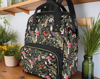 May include: A black backpack with a zippered pocket and a floral pattern featuring mushrooms, ferns, and berries. The pattern is on a dark green background.