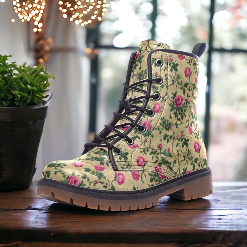 May include: A pair of brown leather boots with a floral pattern featuring pink roses and green leaves on a cream background. The boots have black laces and a brown rubber sole.