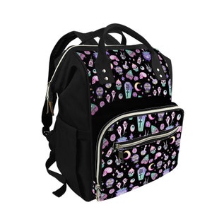 May include: A black diaper bag with a whimsical, gothic-inspired print featuring ghosts, eyeballs, moons, and other spooky elements in pastel colors. The bag has multiple pockets and a zippered closure.