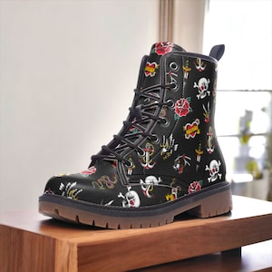 Puede incluir: Botas de cuero negro con cierre de cordones y estampado colorido inspirado en tatuajes, con ancres, corazones, rosas, calaveras y serpientes.