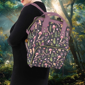 Può includere: Uno zaino viola e verde con una stampa di funghi e fiori. Lo zaino ha un grande scomparto principale e una tasca anteriore più piccola.