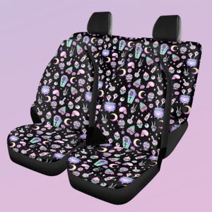 May include: Two black car seat covers featuring a repeating pattern of pastel-colored skulls, ghosts, cauldrons, coffins with the text DO NOT OPEN, crystal balls with the text I SEE GHOSTS, moons, and skeletal hands against a dark background.
