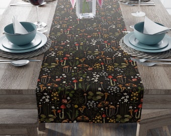 May include: A black table runner with a repeating pattern of mushrooms, flowers, and leaves. The runner is on a wooden table with two place settings on each side.