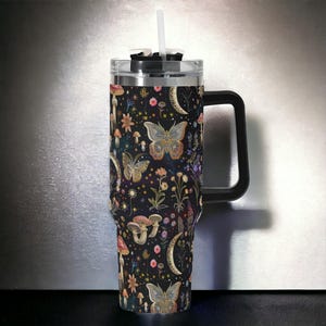 May include: A stainless steel tumbler with a black handle and a lid. The tumbler features a colorful design of butterflies, mushrooms, and flowers on a black background.