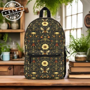 May include: A black backpack with a floral pattern featuring bees and flowers. The backpack has a zippered pocket on the front and adjustable straps.
