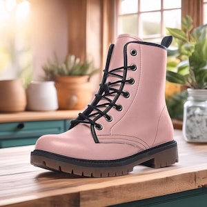 May include: A pink combat boot with black laces and trim. The boot has a lug sole and a pull tab at the back. The boot is made of a smooth material and is set on a wooden surface.