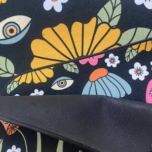 May include: Black and white rug with a retro floral pattern featuring yellow, blue, pink, and white flowers. The rug also has a repeating eye design.