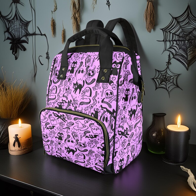 May include: A purple backpack with a black and white print of ghosts, cats, and other Halloween-themed imagery. The backpack has a zippered front pocket and adjustable straps.
