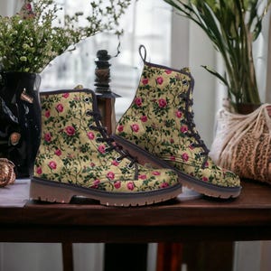 May include: A pair of brown leather boots with a floral pattern featuring pink roses and green leaves on a beige background. The boots have black laces and a brown sole.