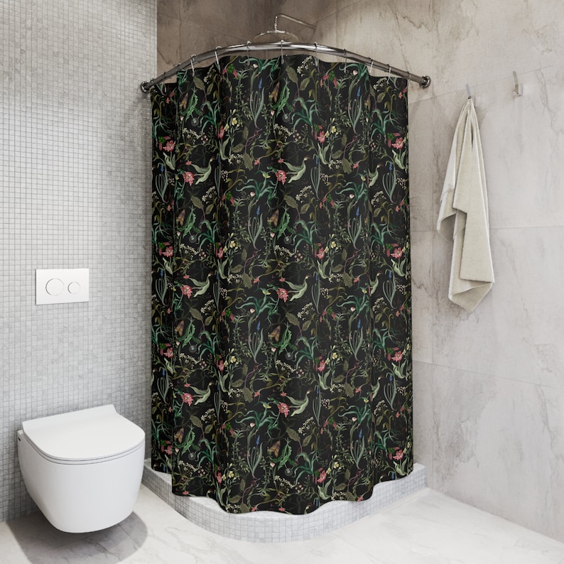 May include: Black shower curtain with a floral pattern featuring green leaves, pink and white flowers, and butterflies. The shower curtain is hanging in a bathroom with a white toilet and gray tiled walls.