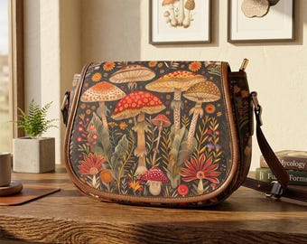 Könnte beinhalten: Schultertasche mit Klappe, mit einem farbenfrohen Pilz- und Blumenmuster auf dunklem Hintergrund. Die Tasche hat eine braune Ledereinfassung und einen Riemen sowie einen goldfarbenen Verschluss. Die Tasche liegt auf einer Holzoberfläche.