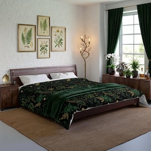 May include: A dark-colored comforter featuring a botanical pattern of green and gold leaves and flowers, topped with a solid dark green throw blanket. The bedding is set on a wooden bed frame with white pillows in a room with white brick walls.