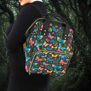 Può includere: Uno zaino nero con un colorato motivo a farfalle e fiori. Lo zaino ha una maniglia superiore, spallacci regolabili e diverse tasche. Il design presenta farfalle nei toni del rosa, blu, giallo e arancione, su uno sfondo scuro.