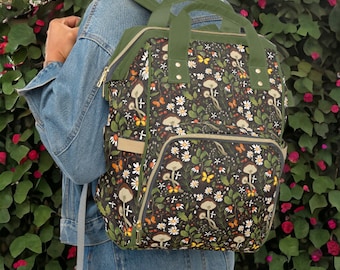 May include: A green backpack with a black and white mushroom and butterfly print. The backpack has multiple pockets and zippers.