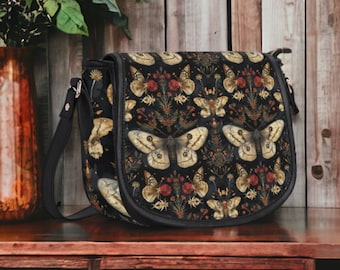 May include: A black leather satchel bag with a floral and butterfly pattern. The bag has a long adjustable strap and a flap closure.
