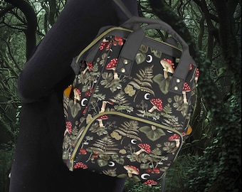 May include: A black backpack with a forest-themed print featuring mushrooms, ferns, and crescent moons. The backpack has a large main compartment and a smaller front pocket.