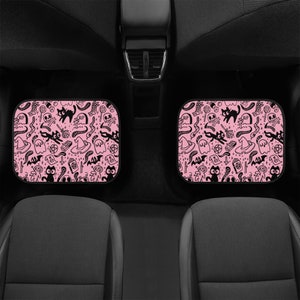 May include: Two pink car seat headrests with a black and white Halloween themed pattern. The pattern includes cats, ghosts, bats, skulls, and other spooky symbols.